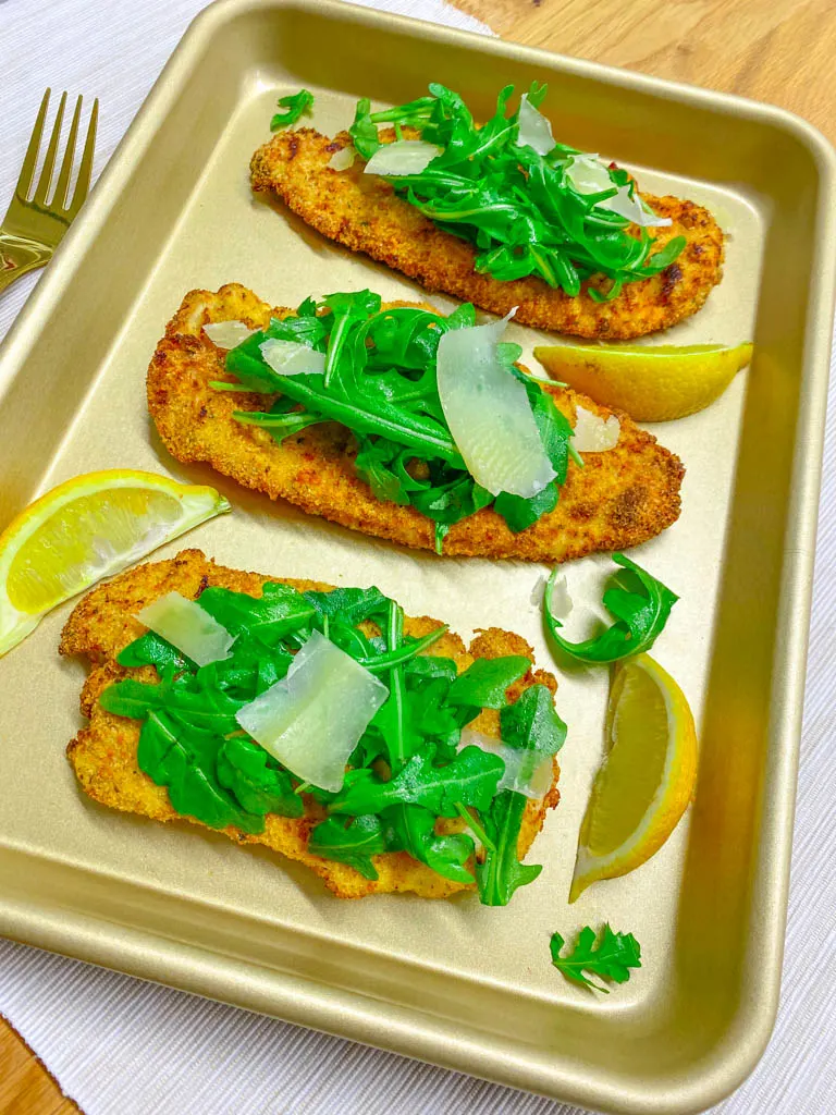 chicken milanese on a sheet pan. chicken cutlets with arugula salad and parmesan and lemon wedges