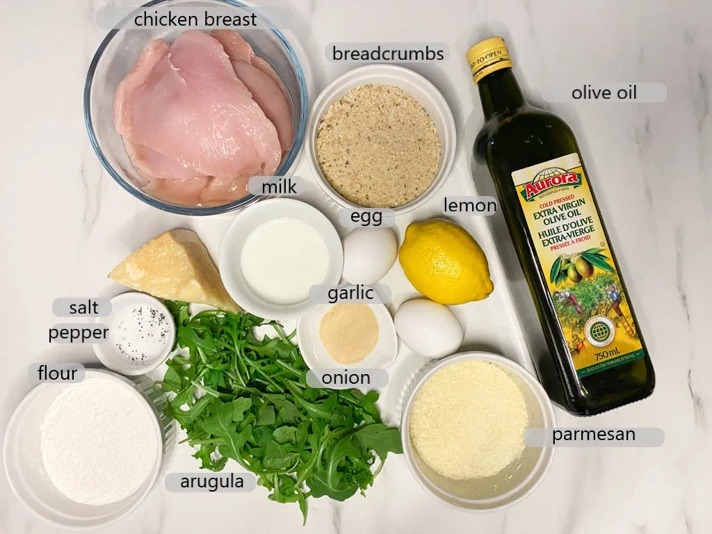 bowls with chicken, breadcrumbs, olive oil, lemon, parmesan, onion, garlic, egg, milk, argula, salt, pepper, flour. ingredients to make chicken milaneses