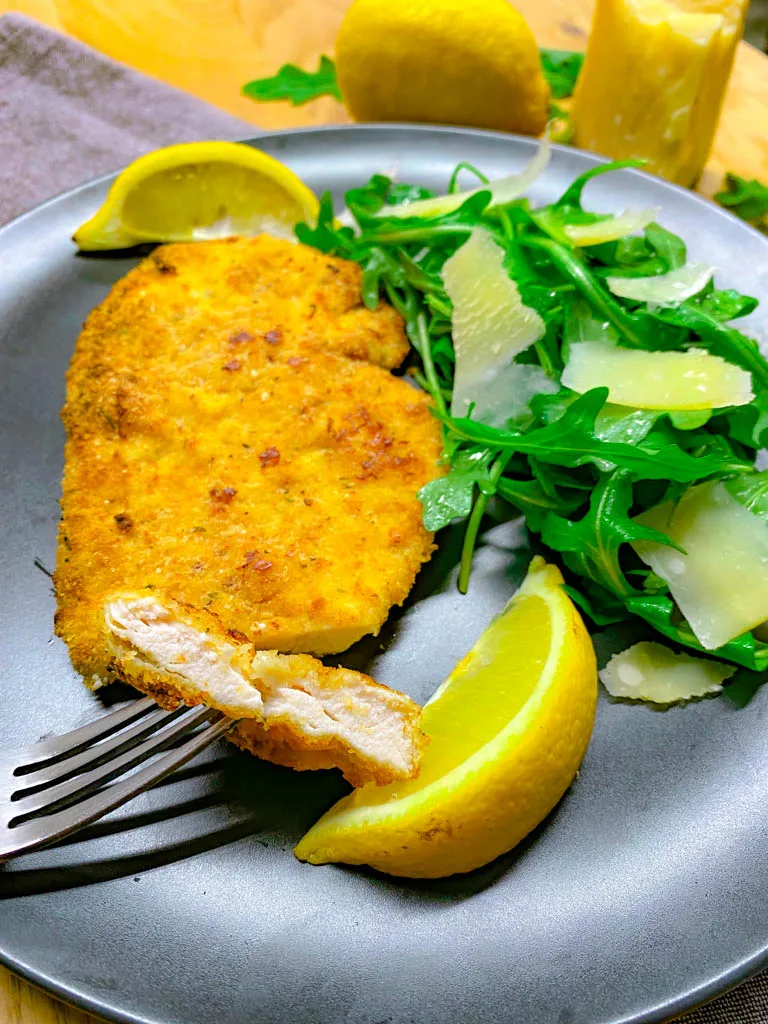 chicken Milanese on a plate with arugula salad and lemon and parmesan around