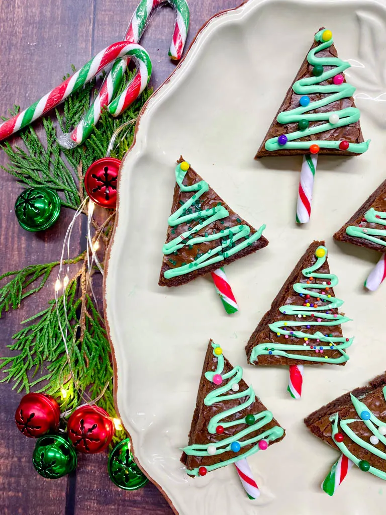 Christmas Tree Brownies plated on a white plate with cedar leaves, bells, candy canes and Christmas lights