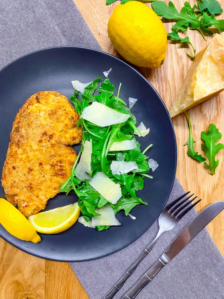chicken Milanese on a plate with arugula salad and lemon and parmesan around