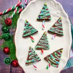 Christmas Tree Brownies plated on a white plate with cedar leaves, bells, candy canes and Christmas lights