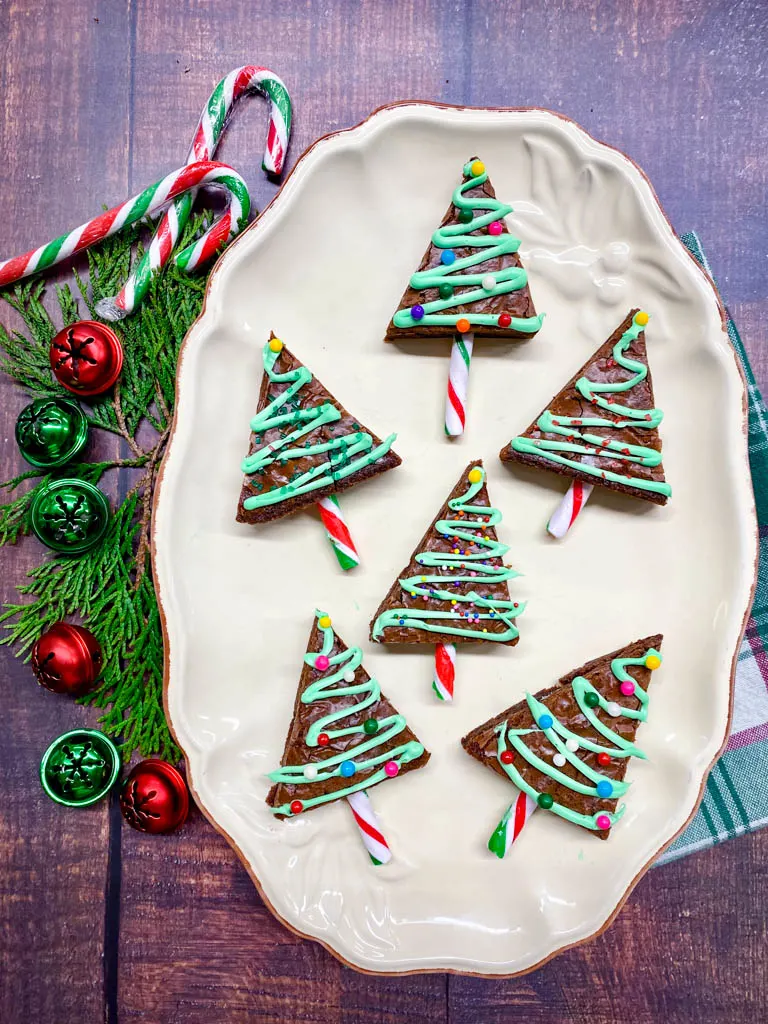 Christmas Tree Brownies plated on a white plate with cedar leaves, bells, candy canes and Christmas lights