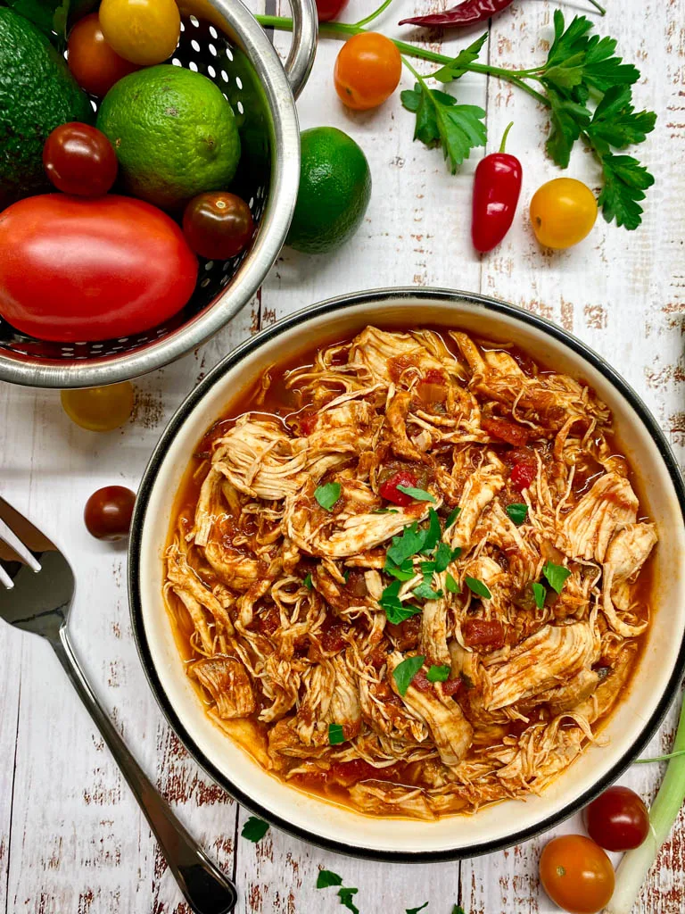 instant pot Mexican shredded chicken in a white bowl with tortillas and green onions