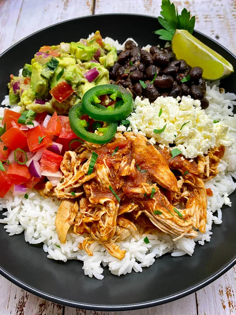 burrito bowl with instant pot Mexican shredded chicken in a black bowl with tortillas and green onions