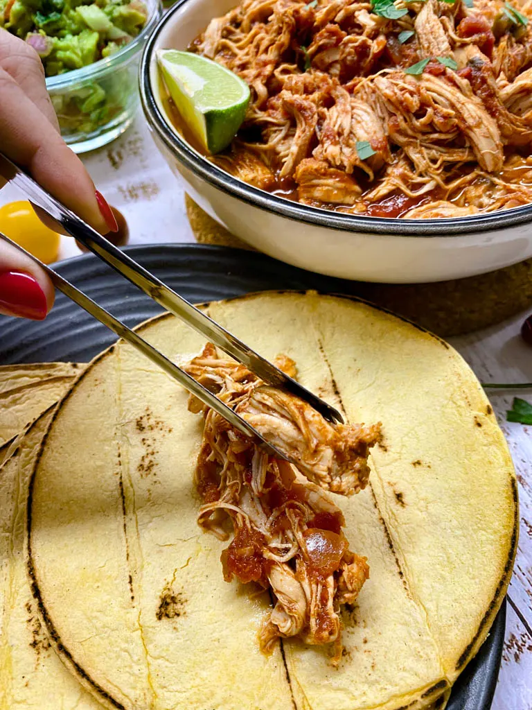 instant pot Mexican shredded chicken in a white bowl with tortillas and green onions making a taco