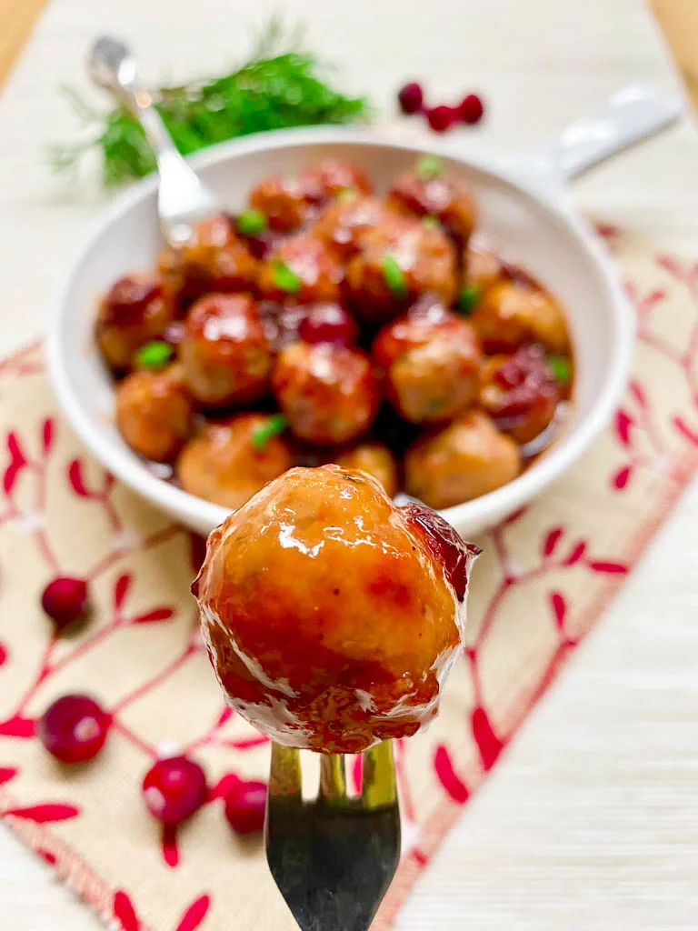 cranberry sweet and sour meatballs plated in a white bowl with a burlap towel