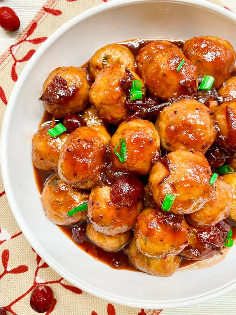 cranberry sweet and sour meatballs plated in a white bowl with a burlap towel