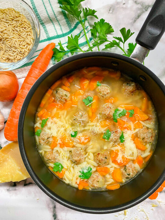 a pot of turkey meatball orzo soup with bread, carrots, onion, garlic, parsley and parmesan cheese around the bowls