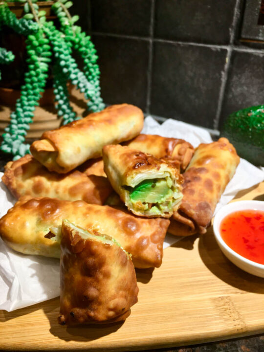 copycat cheesecake factory avocado egg rolls air fried and plated on a wood board