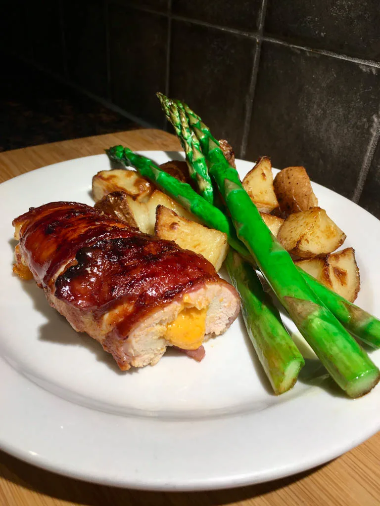 bacon wrapped cheese stuffed bacon plated with asparagus and roasted potatoes