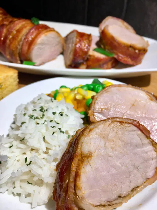 bacon wrapped pork tenderloin plated with rice and mixed vegetables