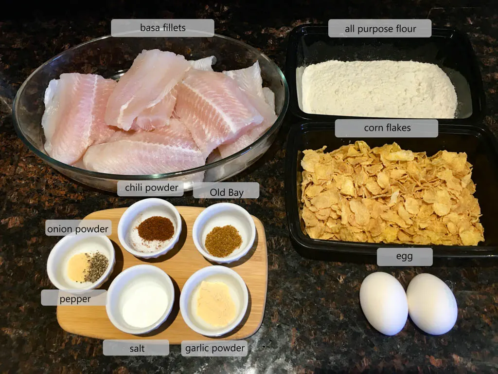 ingredients to make corn flake crusted fish on a wood board