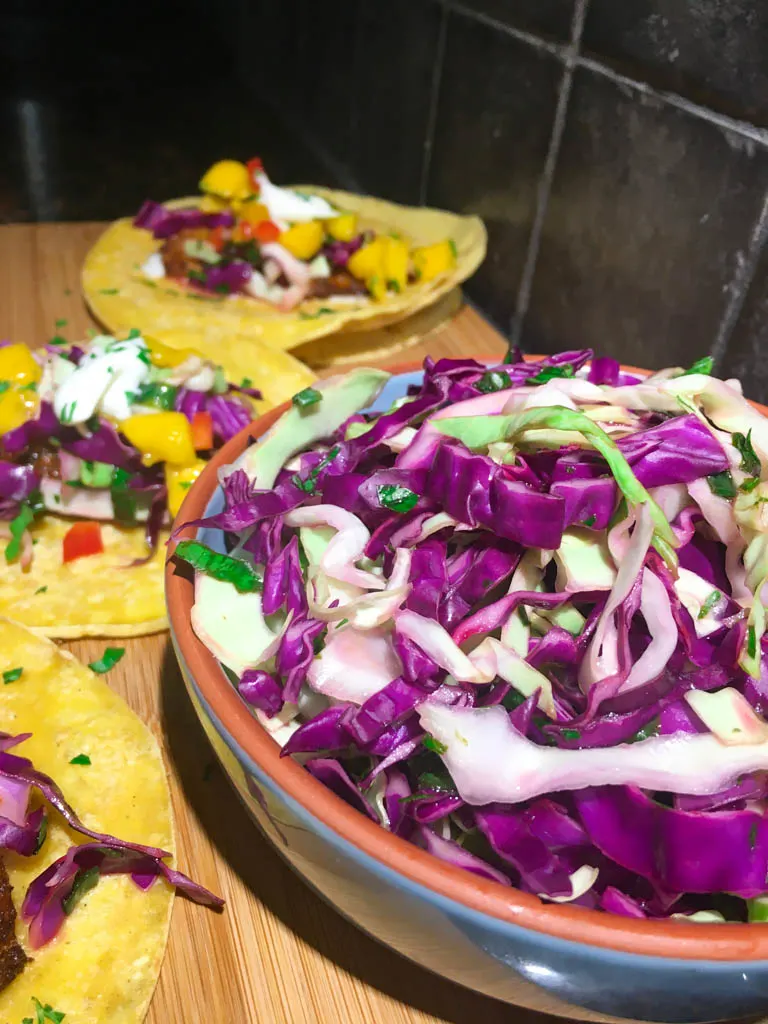 fish tacos plated on a wood board with line, mango salsa, cabbage slaw and lime crema