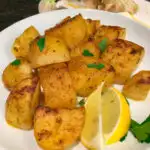 greek roasted potatoes on a white plate with lemon