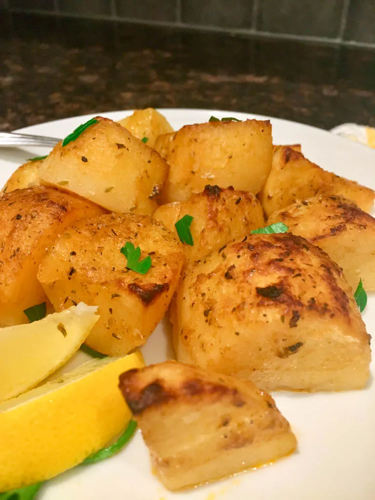 greek roasted potatoes on a white plate with lemon