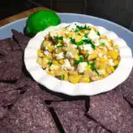 Mexican Street Corn Dip plated with corn chips and a lime