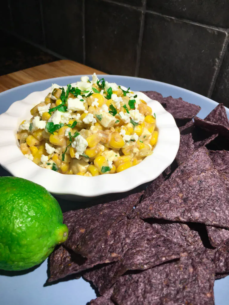 Mexican Street Corn Dip plated with corn chips and a lime