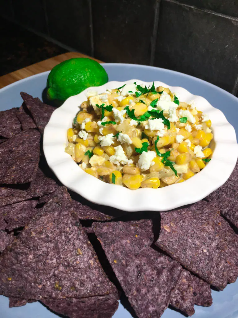 Mexican Street Corn Dip plated with corn chips and a lime