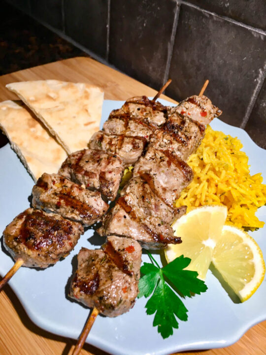 Pork Souvlaki Recipe plated on blue plate with lemon, parsley, pita bread and yellow rice