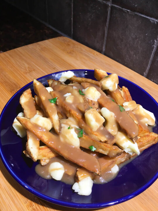 canadian poutine on a blue plate and wood board