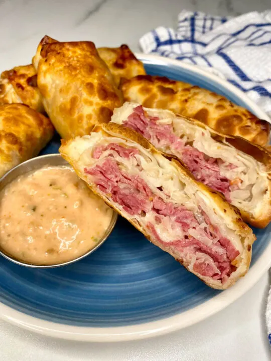 reuben egg rolls on a blue plate with thousand island dipping sauce