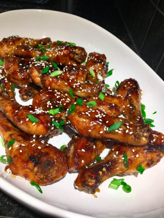 sticky sesame chicken drumsticks legs on a white serving platter