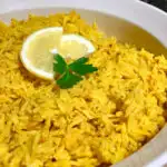 yellow rice in a white serving dish with lemon and parsley