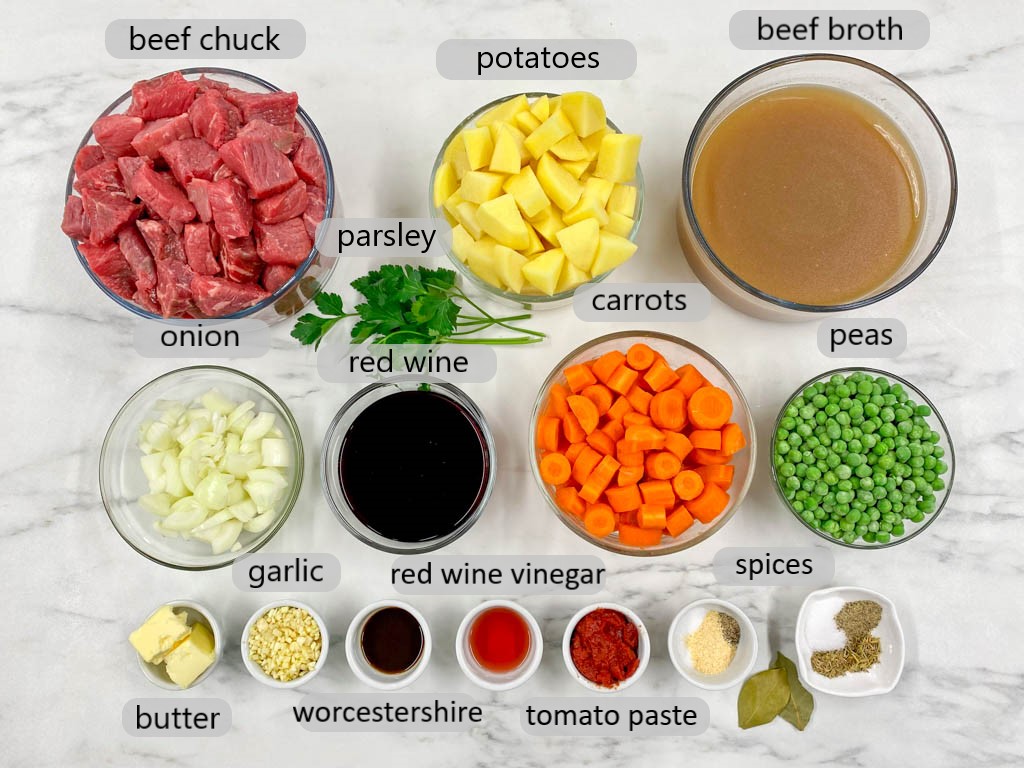 bowls with ingredients to make beef strew (beef chuck, potatoes, onions, carrots, beef broth, red wine, garlic, spices, butter, peas)