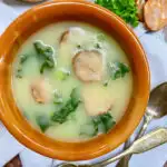 brown bowl of caldo verde portuguese kale soup with bread and spoons