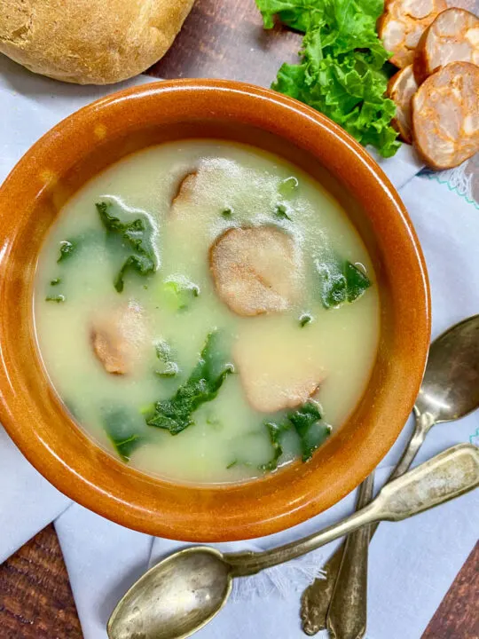 brown bowl of caldo verde portuguese kale soup with bread and spoons