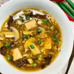 bowl of hot and sour soup with green onions and red chilis on the side