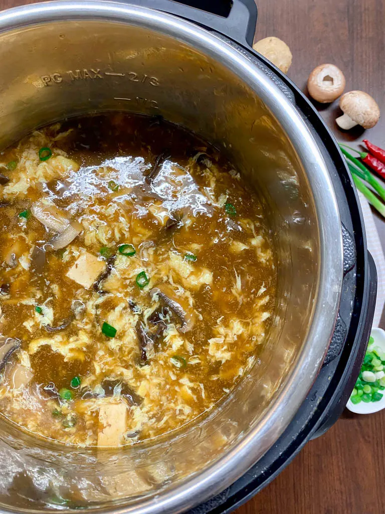 hot and sour soup in an instant pot with mushrooms and green onions on the side