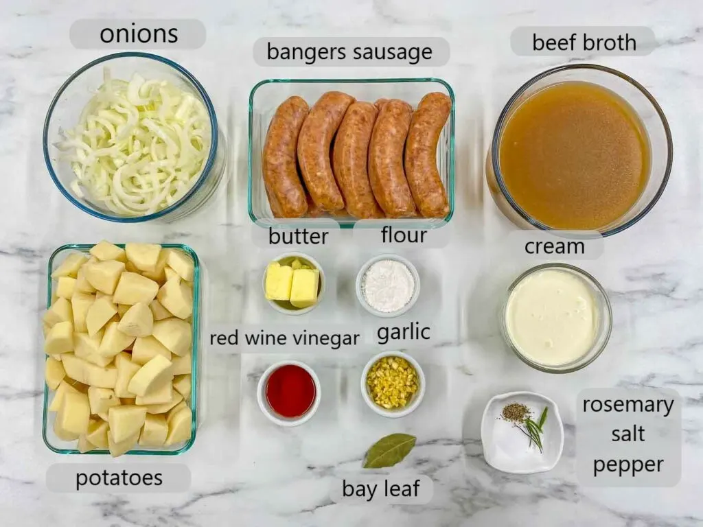 bowl with ingredients for bangers and mash. onions, bangers sausage, beef broth, potatoes, butter, flour, cream, red wine vinegar, garlic, bay leaf, rosemary, salt, pepper