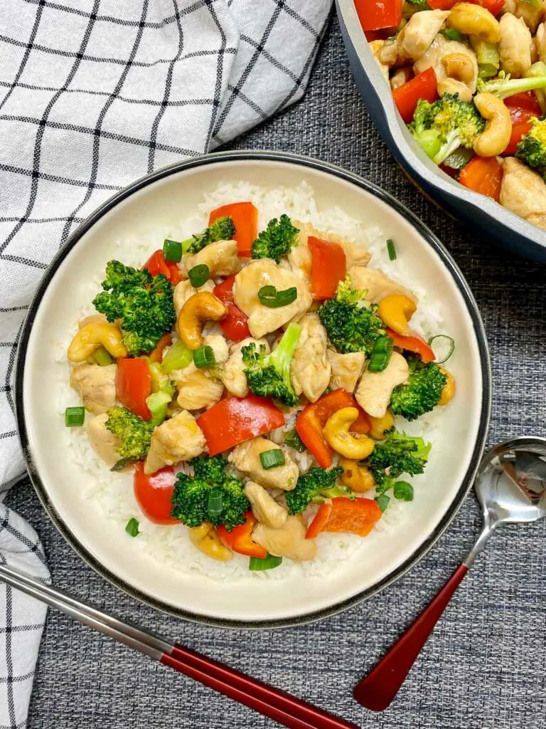 cashew chicken stir fry in a white bowl with cashews and green onions on the side