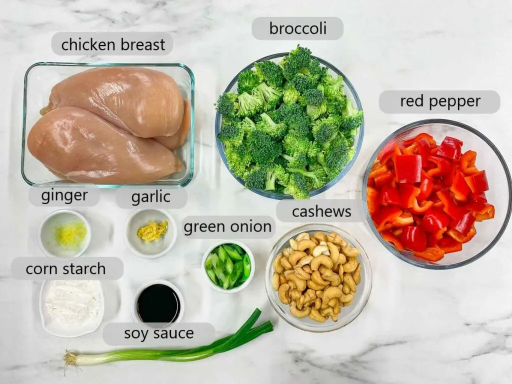 bowls with ingredients to make cashew chicken stir fry (chicken, broccoli, red pepper, cashews, green onion, garlic, ginger, corn starch, soy sauce)