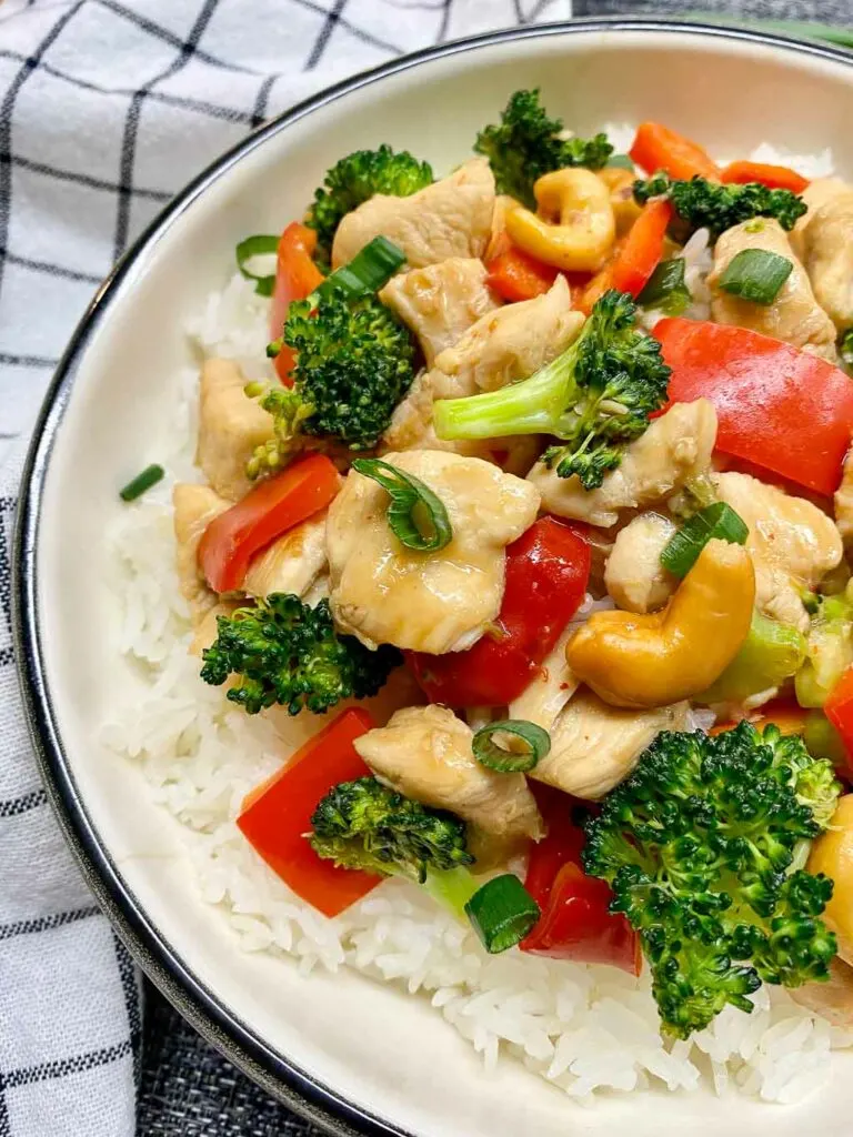 cashew chicken stir fry in a white bowl with cashews and green onions on the side