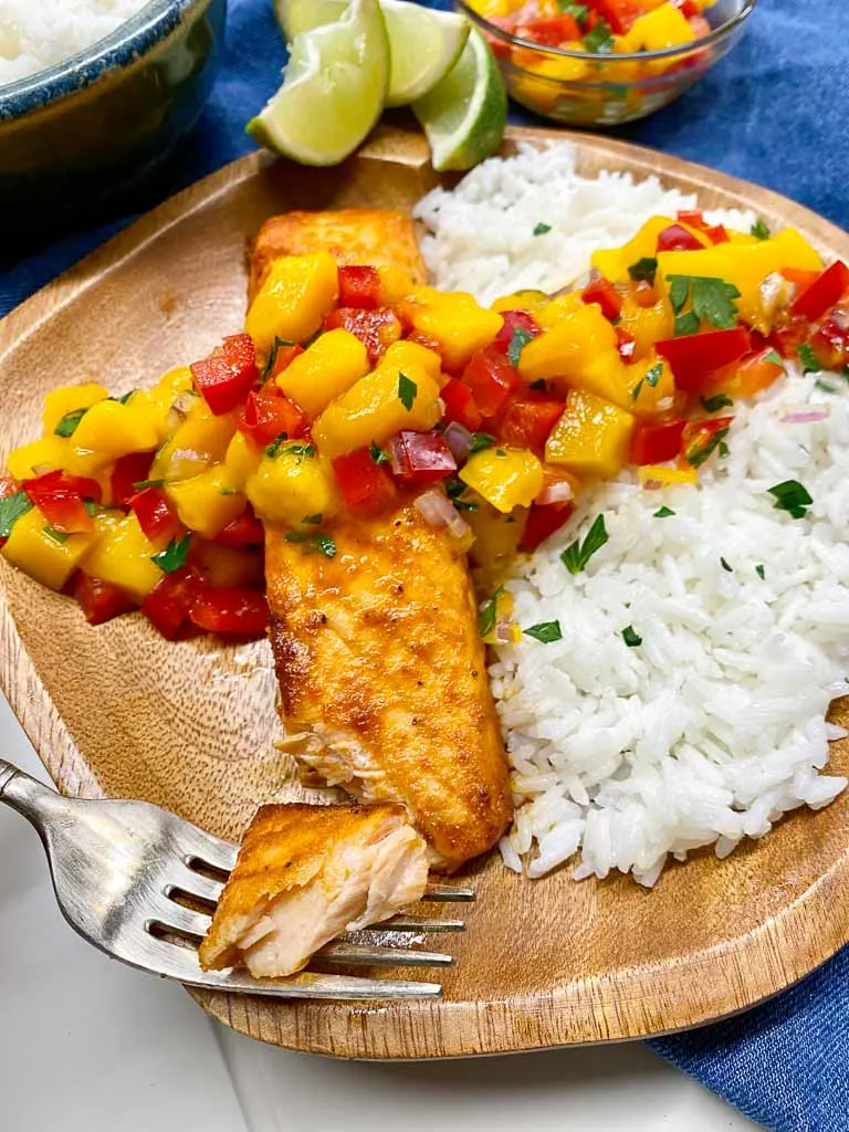 mango salsa salmon with coconut rice on a wood plate and a side of coconut rice and lime