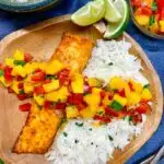 mango salsa salmon with coconut rice on a wood plate and a side of coconut rice and lime