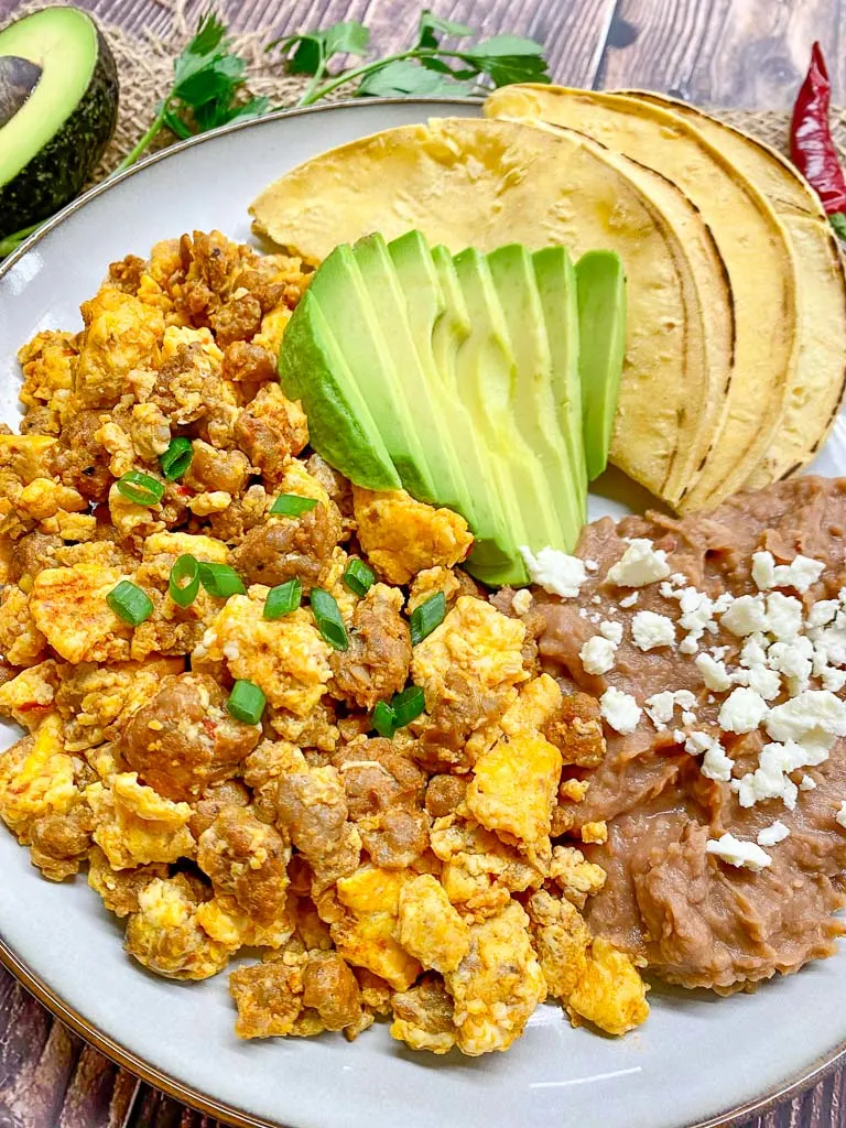 huevos con chorizo (eggs with chorizo) plated with refried beans, avocado and corn tortillas