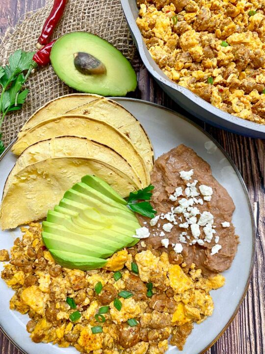 huevos con chorizo (eggs with chorizo) plated with refried beans, avocado and corn tortillas