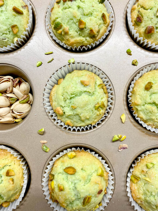 pistachio muffins in a muffin tin with crushed pistachios