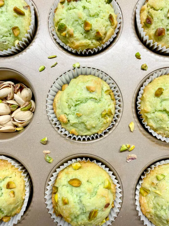 pistachio muffins in a muffin tin with crushed pistachios