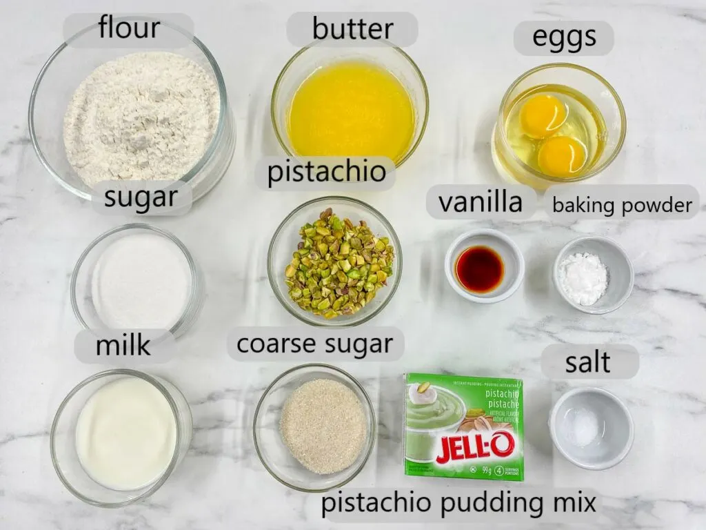 bowls with ingredients, flour, butter, eggs, sugar, pistachio, vanilla, baking powder, milk, coarse sugar, pistachio pudding mix and salt to make pistachio muffins