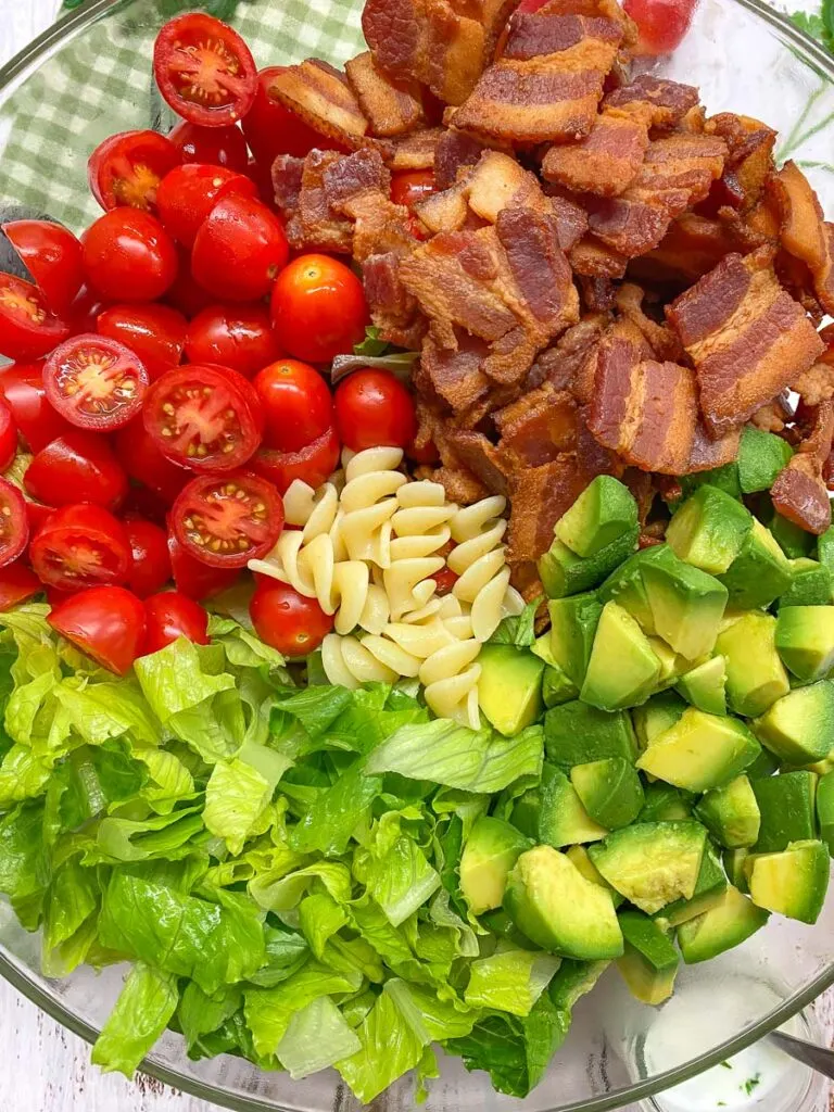 BLT pasta salad in a glass bowl with a side jar of ranch dressing and a green plaid towel