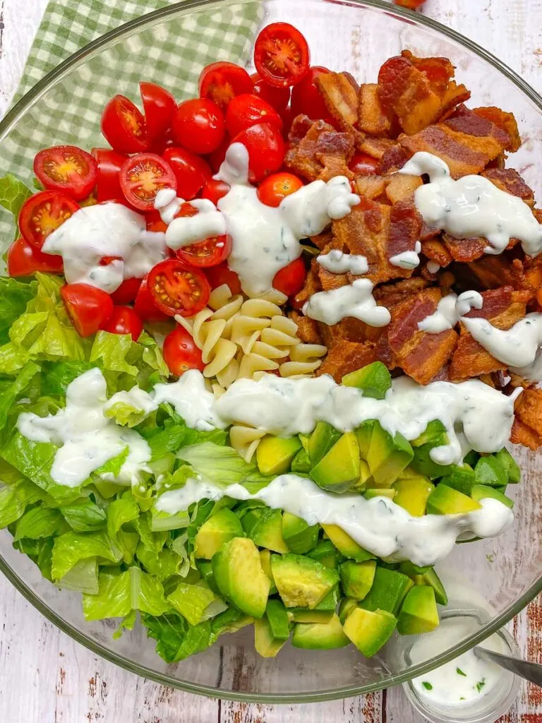 BLT pasta salad in a glass bowl with a side jar of ranch dressing and a green plaid towel