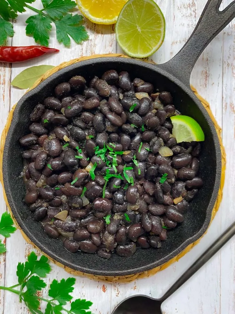 copycat chipotle black beans in a cast iron pan with cilantro and lime garnish