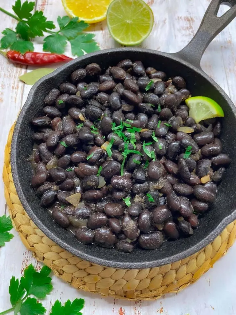 copycat chipotle black beans in a cast iron pan with cilantro and lime garnish