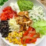 chipotle copycat recipe pollo asado bowl with corn salsa, black beans, cilantro lime rice, and toppings in a white bowl