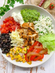chipotle copycat recipe pollo asado bowl with corn salsa, black beans, cilantro lime rice, and toppings in a white bowl